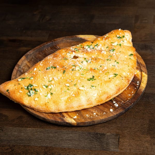 Golden-brown Baba Dough calzone, topped with garlic, parsley, and parmesan, on a wooden board.