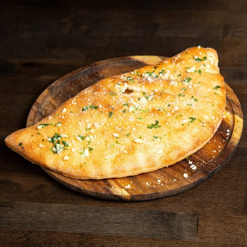 Golden brown garlic bread calzone, topped with parmesan and parsley, on a rustic wooden board.