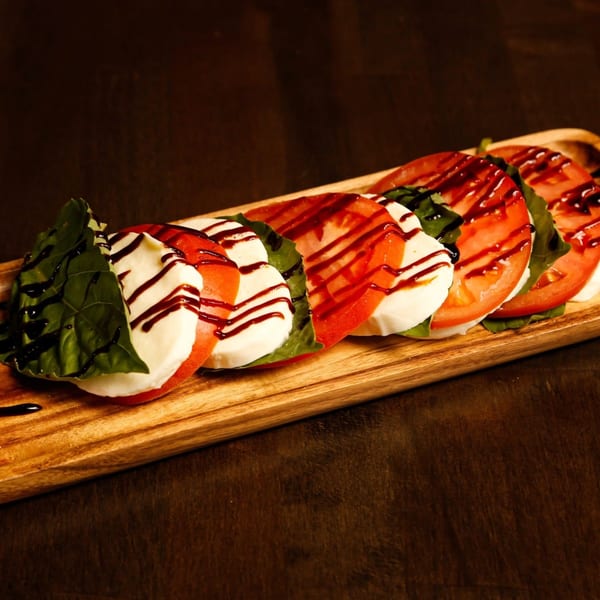 Caprese salad with sliced tomatoes, mozzarella, basil, and balsamic glaze on a wooden board.