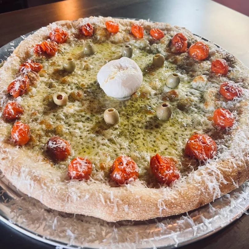 Baba Dough Pizza with pesto, cherry tomatoes, olives, and a dollop of burrata cheese.